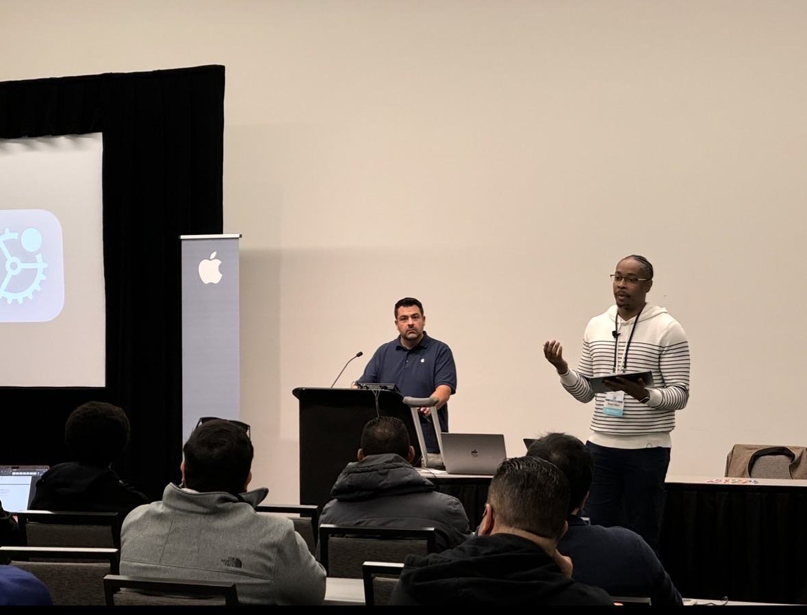Kenan presenting on stage alongside a colleague at a technology session